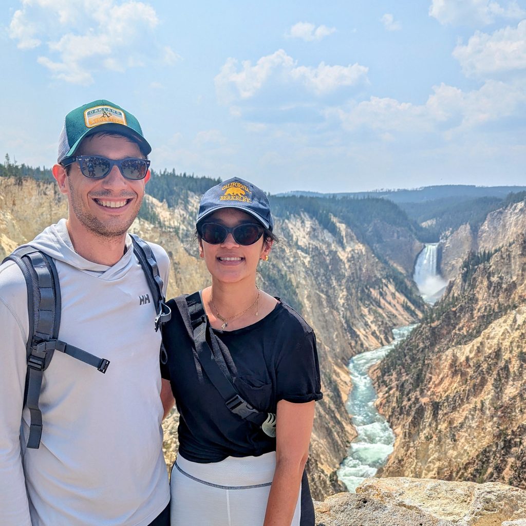 Henry De Belly stands with his arm around his partner and the Grand Canyon of the Yellowstone behind them.